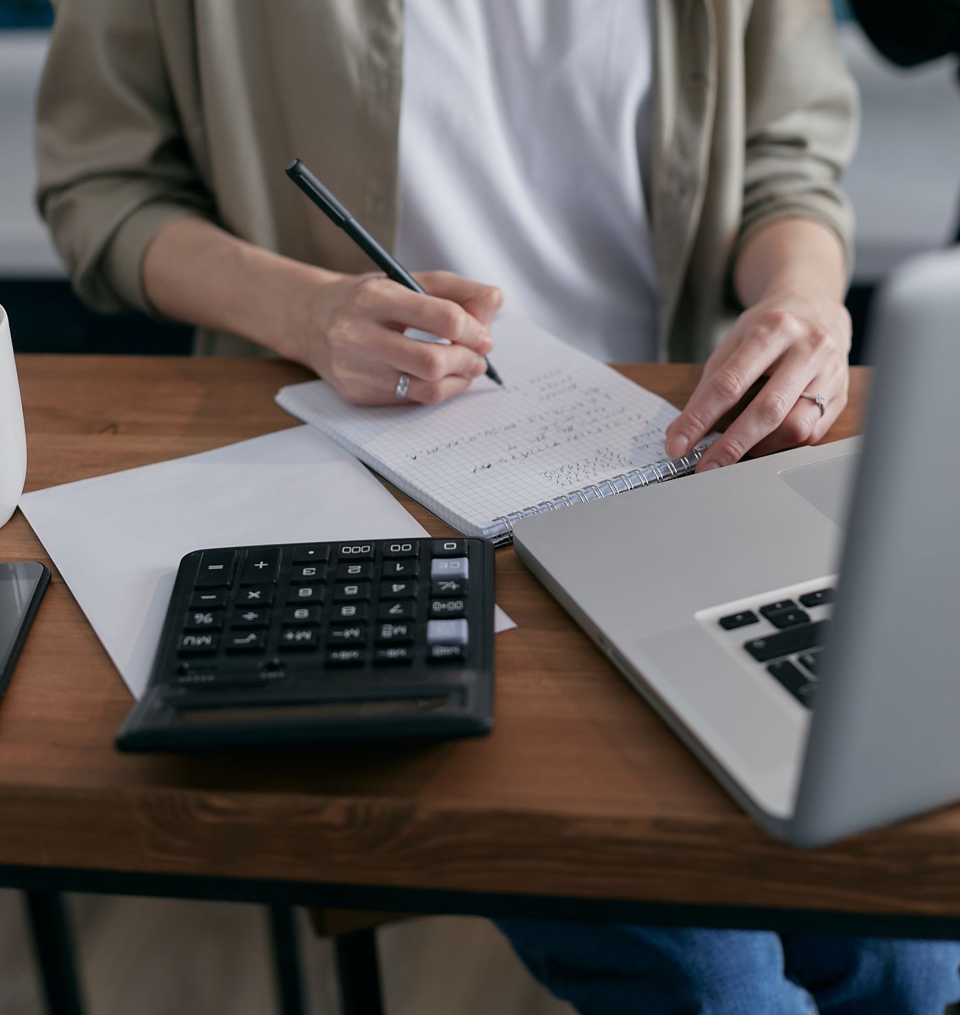 Pessoa a organizar apontamentos com um caderno, uma calculadora e um computador portátil